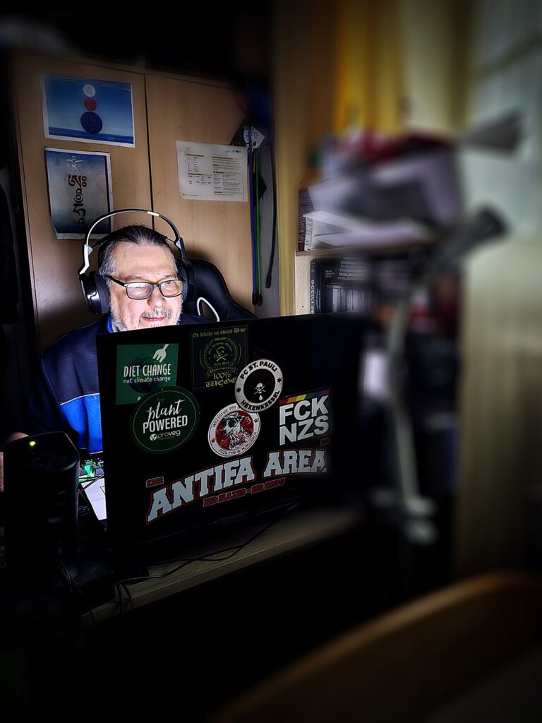 Piotr Krupa w sluchawkach przy laptopie oklejonym naklejkami